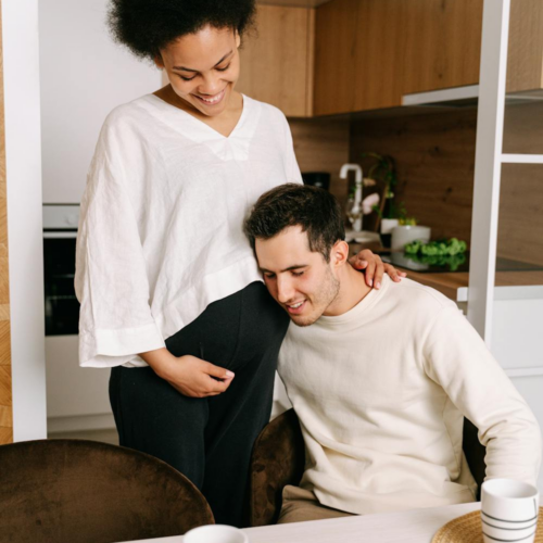 photo of a guy sitting down hugging his pregnant wife. How to save money on maternity leave